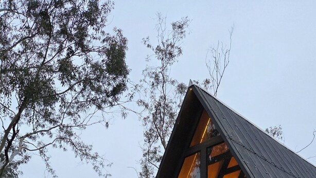 A cabin with a sloped roof, wooden deck, and a staircase leading to the entrance. - A retreat at Chalé A-Frame Parobé, with a lake, fire pit, and grill. (Poço Fundo)