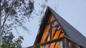 A triangular wooden structure with a deck, surrounded by vegetation. - A retreat at Chalé A-Frame Parobé, with a lake, fire pit, and grill. (Poço Fundo)