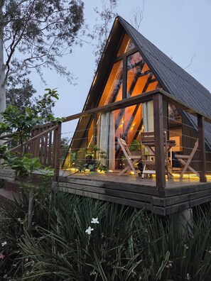 A triangular wooden structure with a deck, surrounded by vegetation. - A retreat at Chalé A-Frame Parobé, with a lake, fire pit, and grill. (Poço Fundo)