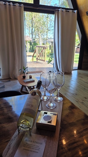 A table with a bottle of wine, glasses, and a box labeled 'Ferrero Rocher' in a room with wooden flooring and a view of an outdoor deck.