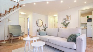 Una sala de estar moderna con un sofá, dos taburetes blancos, una silla, un espejo redondo y una escalera.