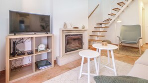 Una sala de estar con chimenea, un televisor sobre un mueble, una escalera y un sillón.