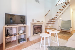 Ein Wohnzimmer mit Kamin, Fernseher auf einem Schrank, einer Treppe und einem Sessel.