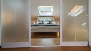 Un dormitorio con tragaluz, una cama con almohadas y una mesita de noche con lámpara.