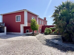 A red building with a cobblestone courtyard, a small tree, and a palm tree. - Villa Tagus Gardians (Trafaria)