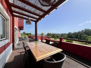 A wooden deck with a table and chairs, a wicker basket, and a view of the landscape. - Villa Tagus Gardians (Trafaria)