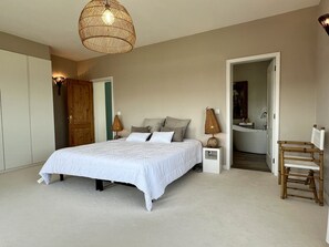 A bedroom with a bed, bedside lamps, a chair, and a bathroom visible through an open door.