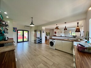 A spacious kitchen with wooden flooring, a built-in washing machine, and pendant lighting.