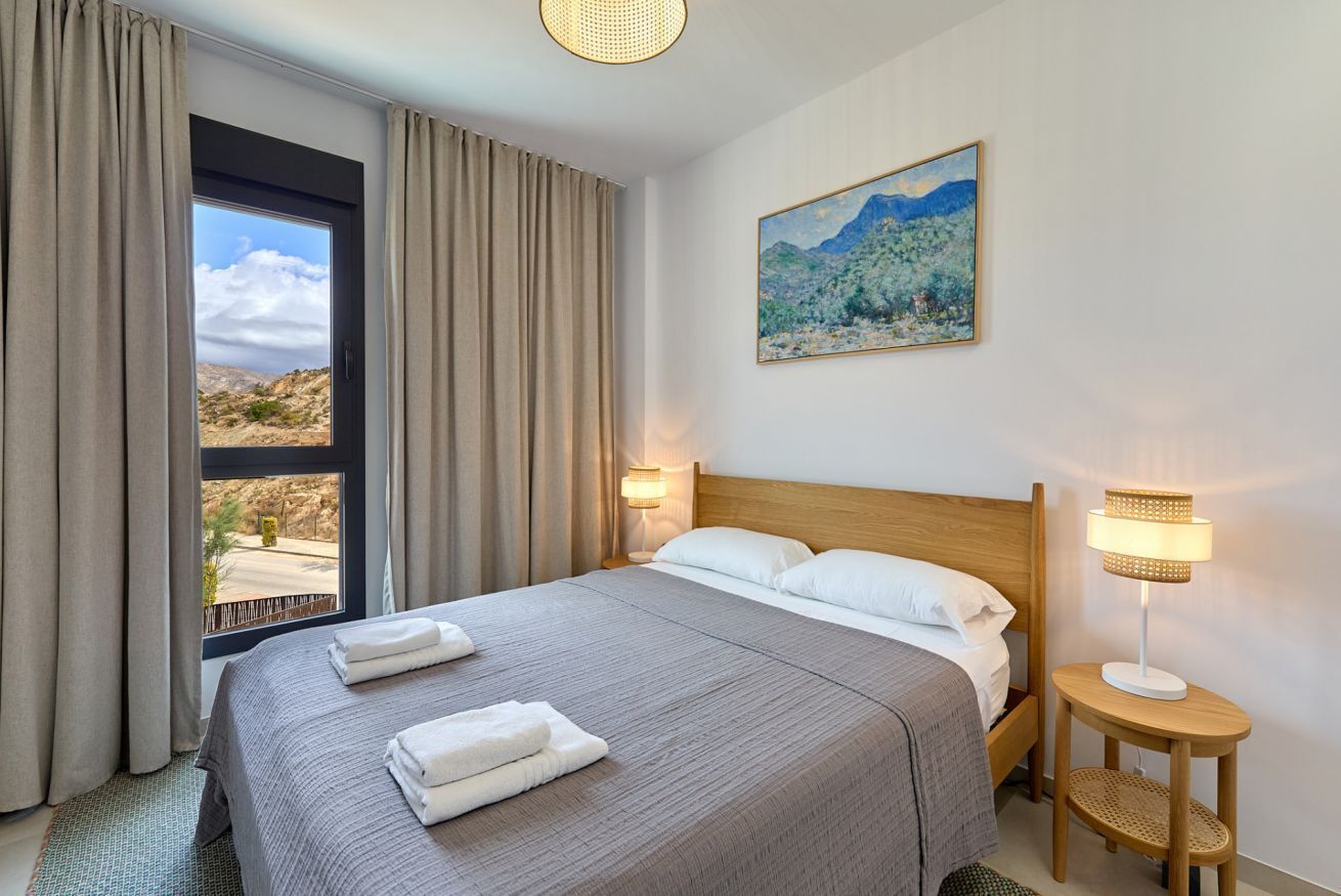 A hotel room with a large bed, two bedside lamps, a painting on the wall, and a window with curtains.