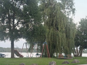 Ein Park mit Schaukeln, einer Rutsche und einer großen Weidweide.