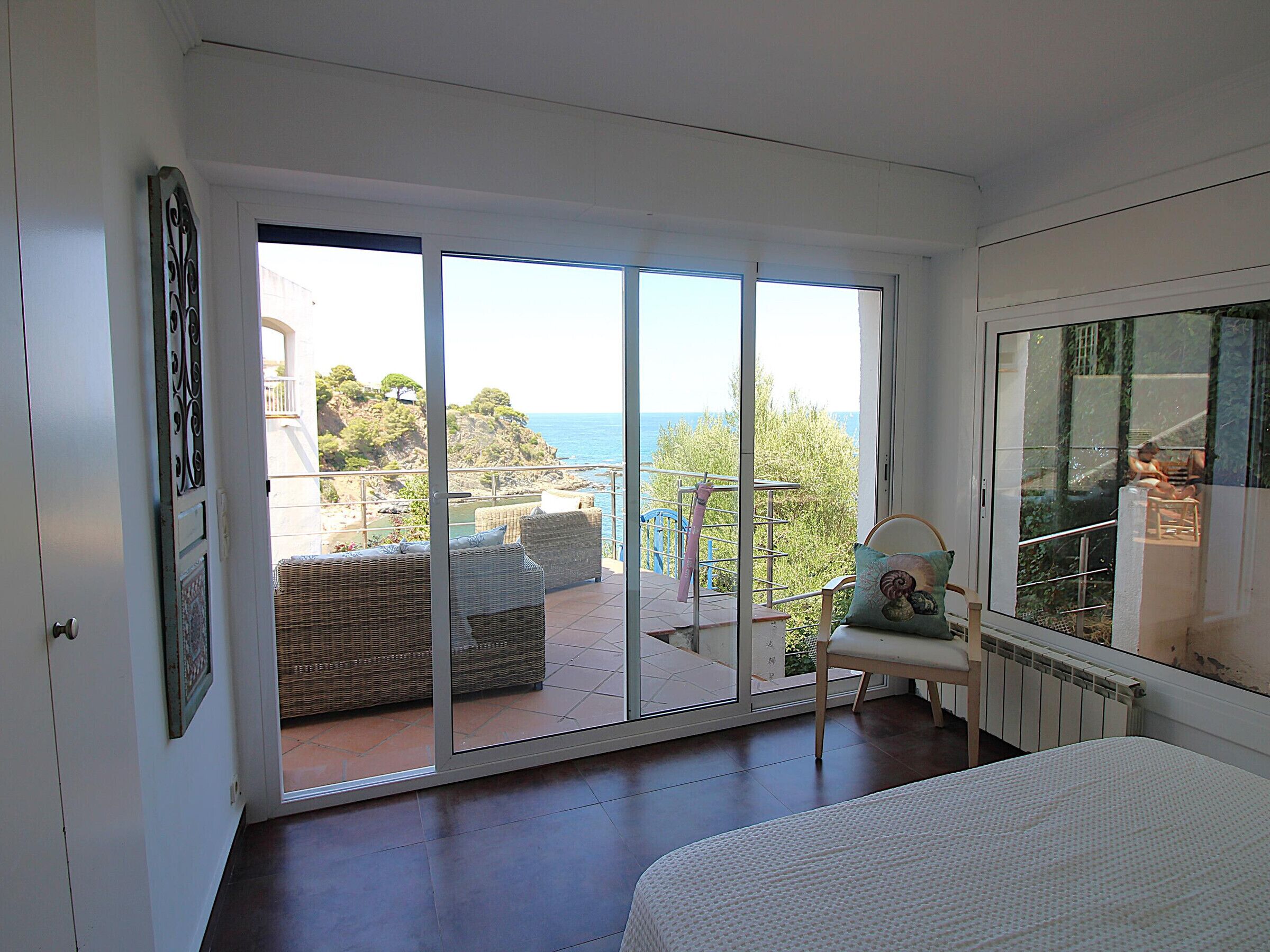 Quarto com uma grande porta de correr de vidro que dá para uma varanda com mobiliário e vista para o mar.