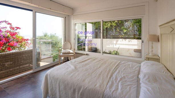 Un dormitorio con una cama grande, una silla, una mesa y vistas a un área exterior con plantas a través de una puerta corredera.