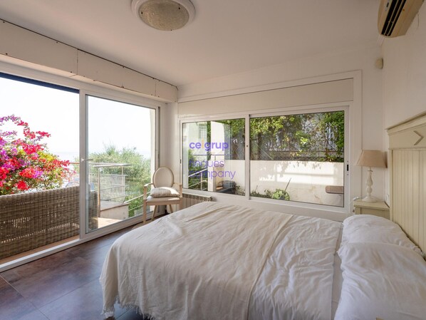 A bedroom with a large bed, a chair, a table, and a view through a sliding door to an outdoor area with plants. - House with sea view, pets allowed - 8 guests (Llançà)