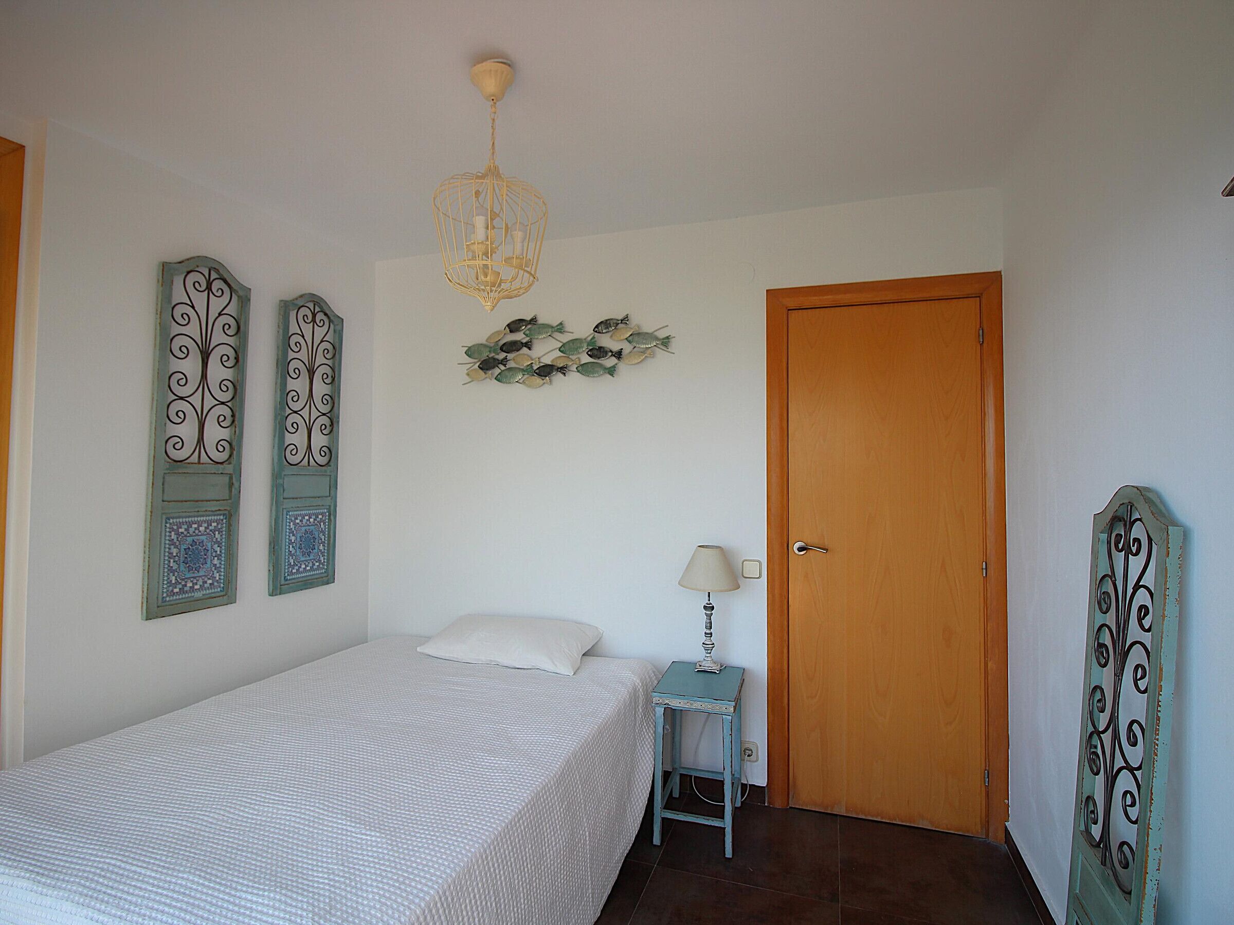 A bedroom with a bed, a bedside table with a lamp, a wooden door, and decorative wall art.