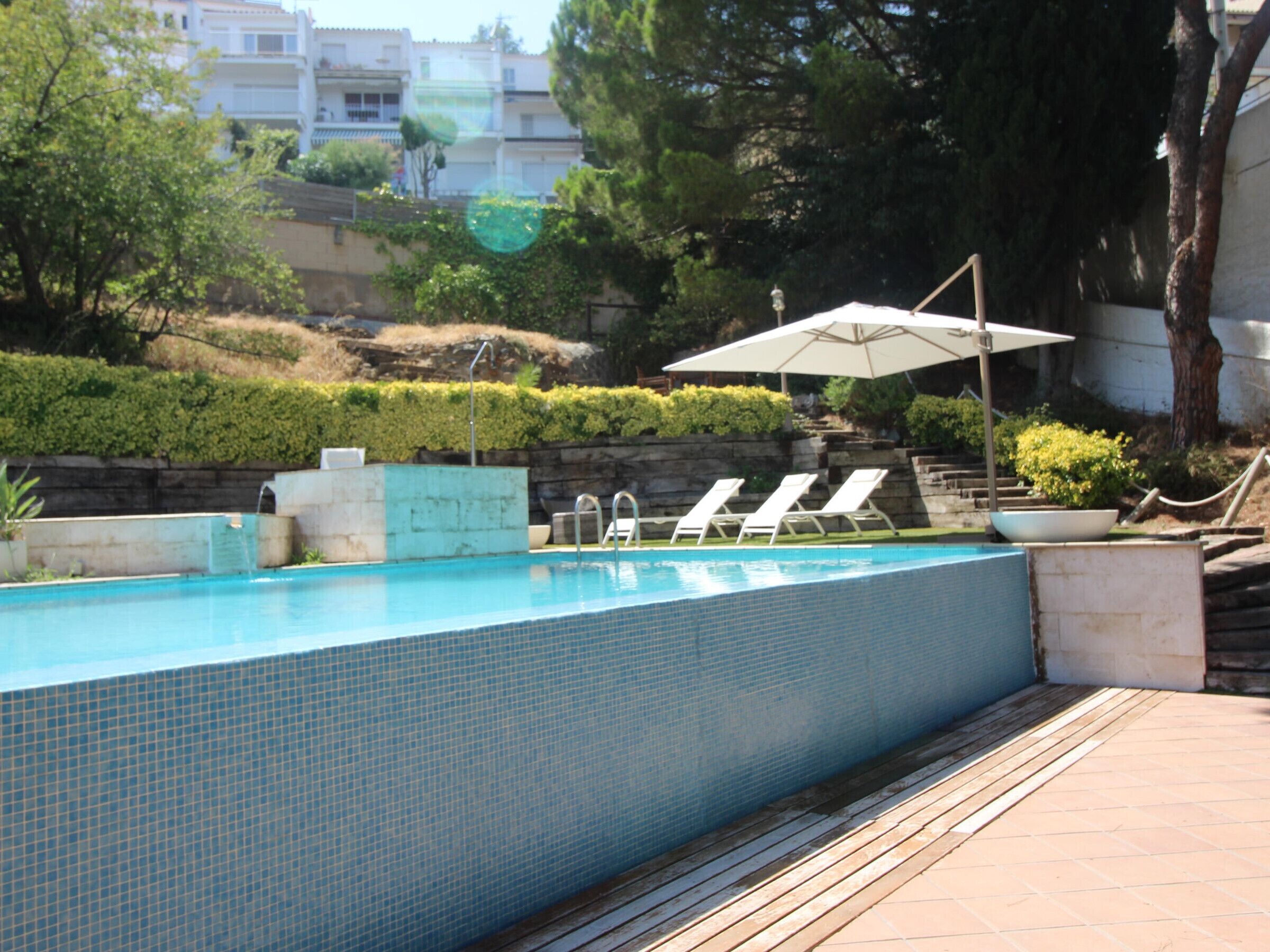 A swimming pool with tiled walls, a wooden deck, and white lounge chairs.