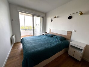 Ein Schlafzimmer mit Bett, Nachttisch, Kommode, Deckenleuchte und Blick durch eine Schiebetür.