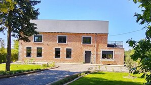 A two-story brick building with a flat roof, a front door, and a small balcony. - Cottage with air conditioning, garden - 6 guests (Taisnières-en-Thiérache)