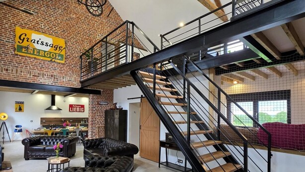 A loft-style room with exposed brick walls, a staircase, and a dining area. - Cottage with air conditioning, garden - 6 guests (Taisnières-en-Thiérache)