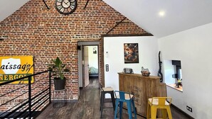 A rustic interior with a brick wall, a clock, a bar area, and a staircase. - Cottage with air conditioning, garden - 6 guests (Taisnières-en-Thiérache)