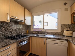 A kitchen with granite countertops, a stove, a dishwasher, and a window with a view of buildings. - Splendid house, sea view - 6 guests (Llançà)
