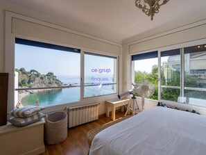 A bedroom with a large window overlooking a coastal view, a bed, a desk, and a standing fan. - Splendid house, sea view - 6 guests (Llançà)