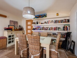 Une pièce comprenant une table à manger, des chaises en osier, un luminaire suspendu et des étagères remplies de livres.