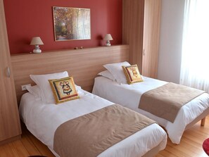 A hotel room with two beds, a red wall, and a painting above the beds.
