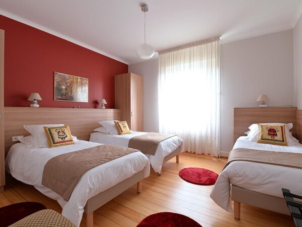 A hotel room with two beds, a red accent wall, a painting, and a large window with curtains.