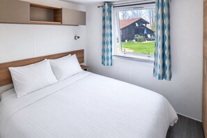 Ein Schlafzimmer mit einem Bett, einem Holzkopfende, einem Fenster mit Vorhängen und einem kleinen Regal über dem Bett.