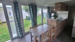 Een compacte keuken met een eettafel en stoelen, een klein aanrecht en uitzicht op een gazon door grote schuifdeuren.