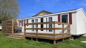 Een stacaravan met terras, zitplaatsen buiten en een omheind gebied.