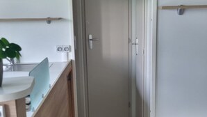 Een smalle gang met een houten vloer, een witte deur aan het einde, en een kitchenette met een spoelbak en aanrecht aan de linkerkant.