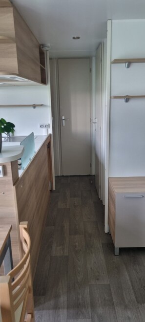 Ein schmaler Flur mit Holzboden, einer weißen Tür am Ende und einer Küchenzeile mit Spüle und Arbeitsplatte auf der linken Seite.