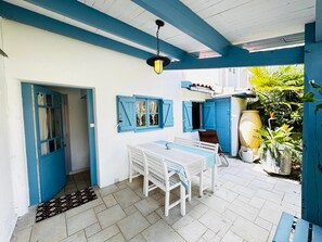 Un espace patio avec une table et des chaises, une porte bleue et un luminaire suspendu.