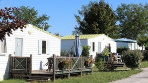 A row of white mobile homes with green roofs, a wooden deck, and a covered seating area with a blue umbrella. - Mobile home, pets OK, AC - 6 guests (Verteillac)