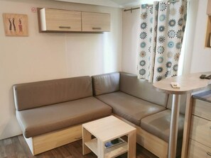 A modern living space with a brown sofa, a small wooden table, a cabinet, and a patterned curtain. - Mobile home, pets OK, AC - 6 guests (Verteillac)