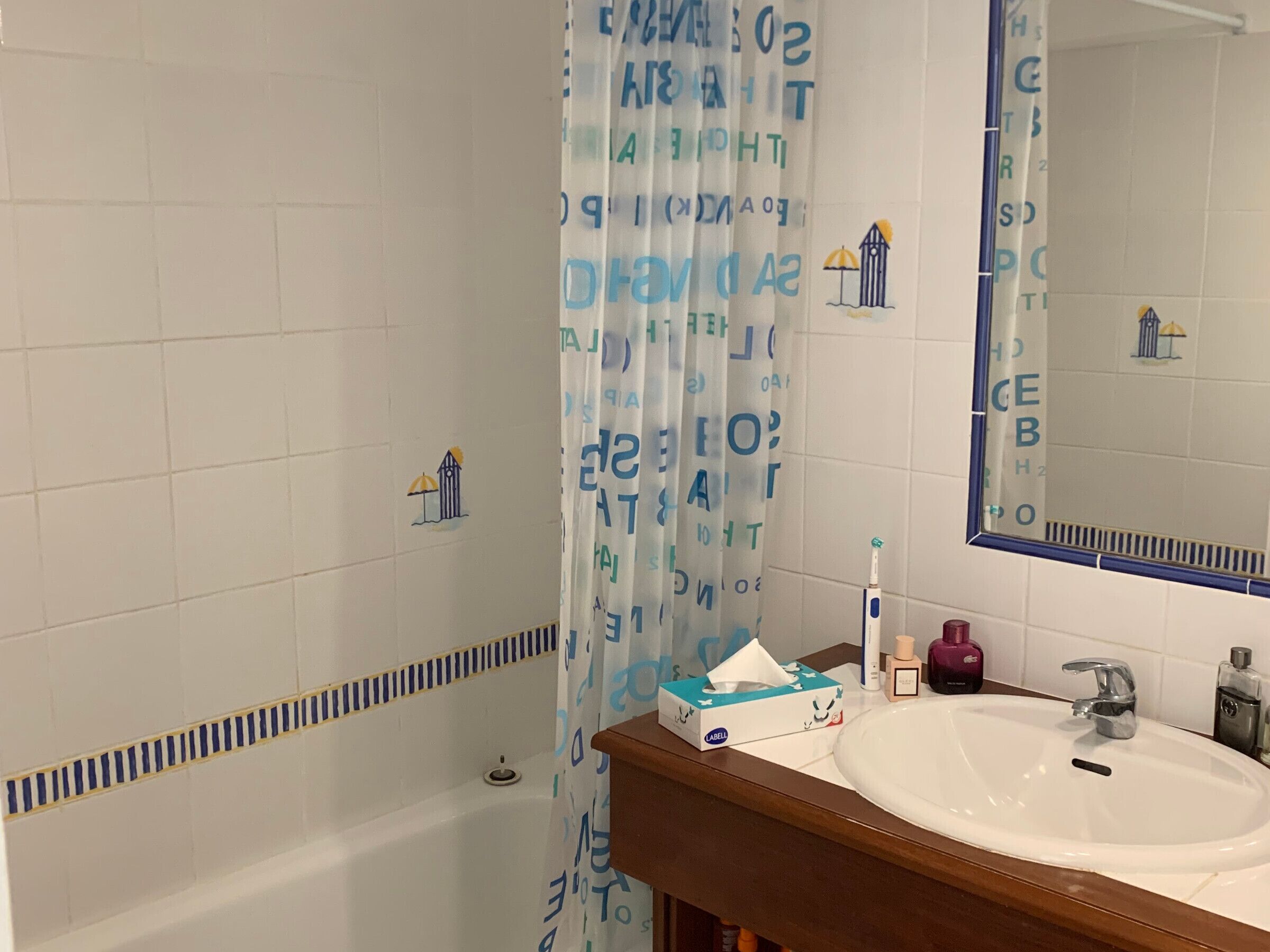 A bathroom with a white sink, a mirror, a towel rack, and a shower curtain with blue text.