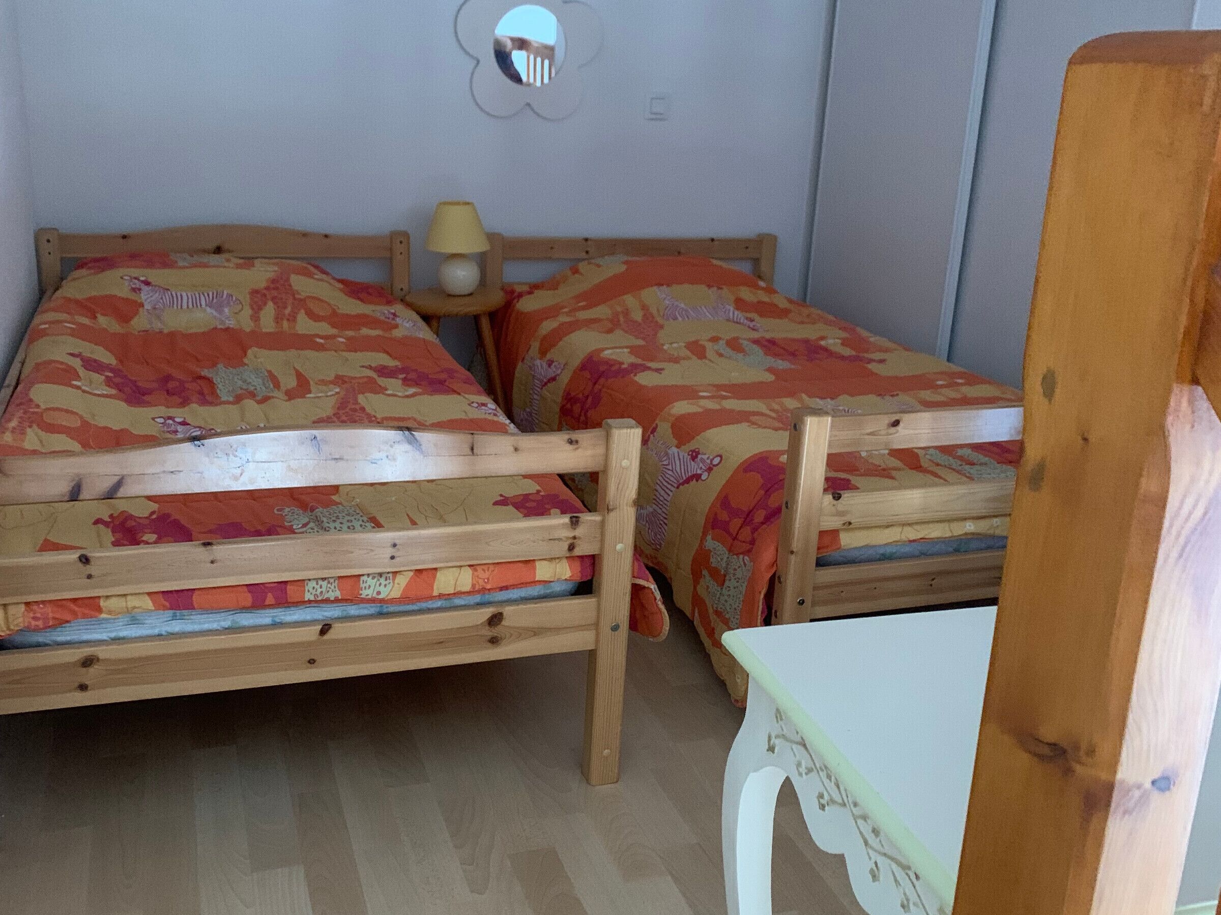 A room with two wooden beds, a small table, and a wall-mounted mirror.