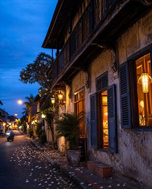 Une rue bordée de bâtiments traditionnels, dont certains sont dotés de balcons et de grandes fenêtres, sous un ciel crépusculaire.