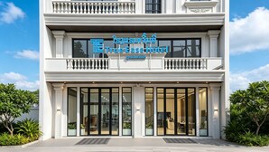 En bygning i to etager med balkon, store vinduer og et skilt der siger 'True Ease Hotel'.