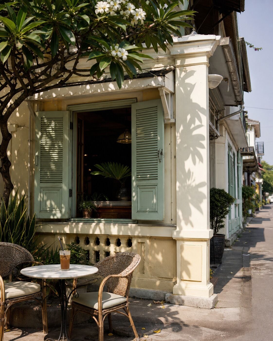 A café with outdoor seating, a table with chairs, and a window with shutters.