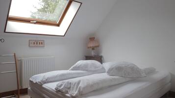 Une chambre avec un puits de lumière, un radiateur, une table de chevet avec une lampe et un lit avec une literie blanche.
