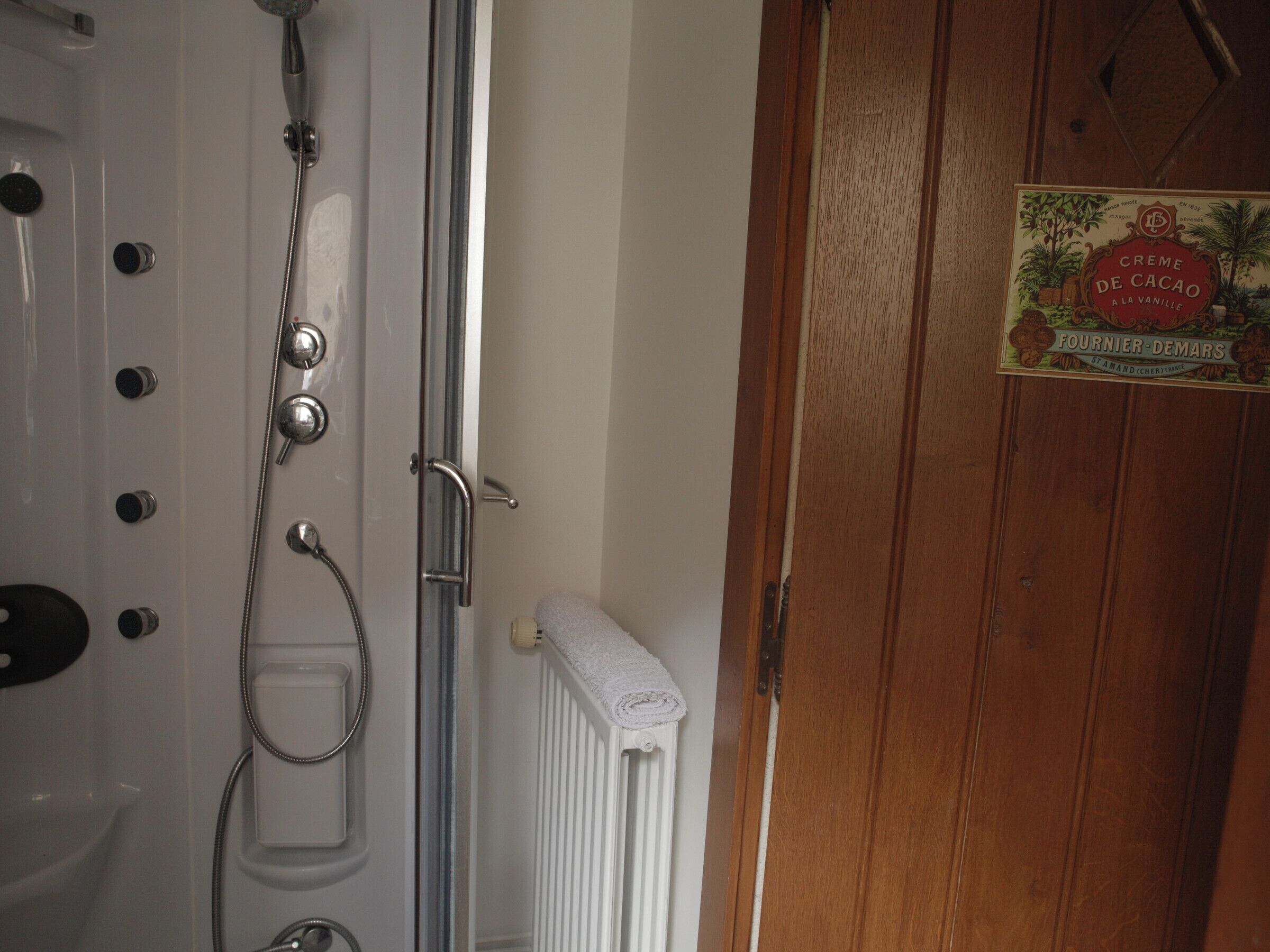 Een badkamer met een douche, een handdoekhouder en een houten deur met een bordje.