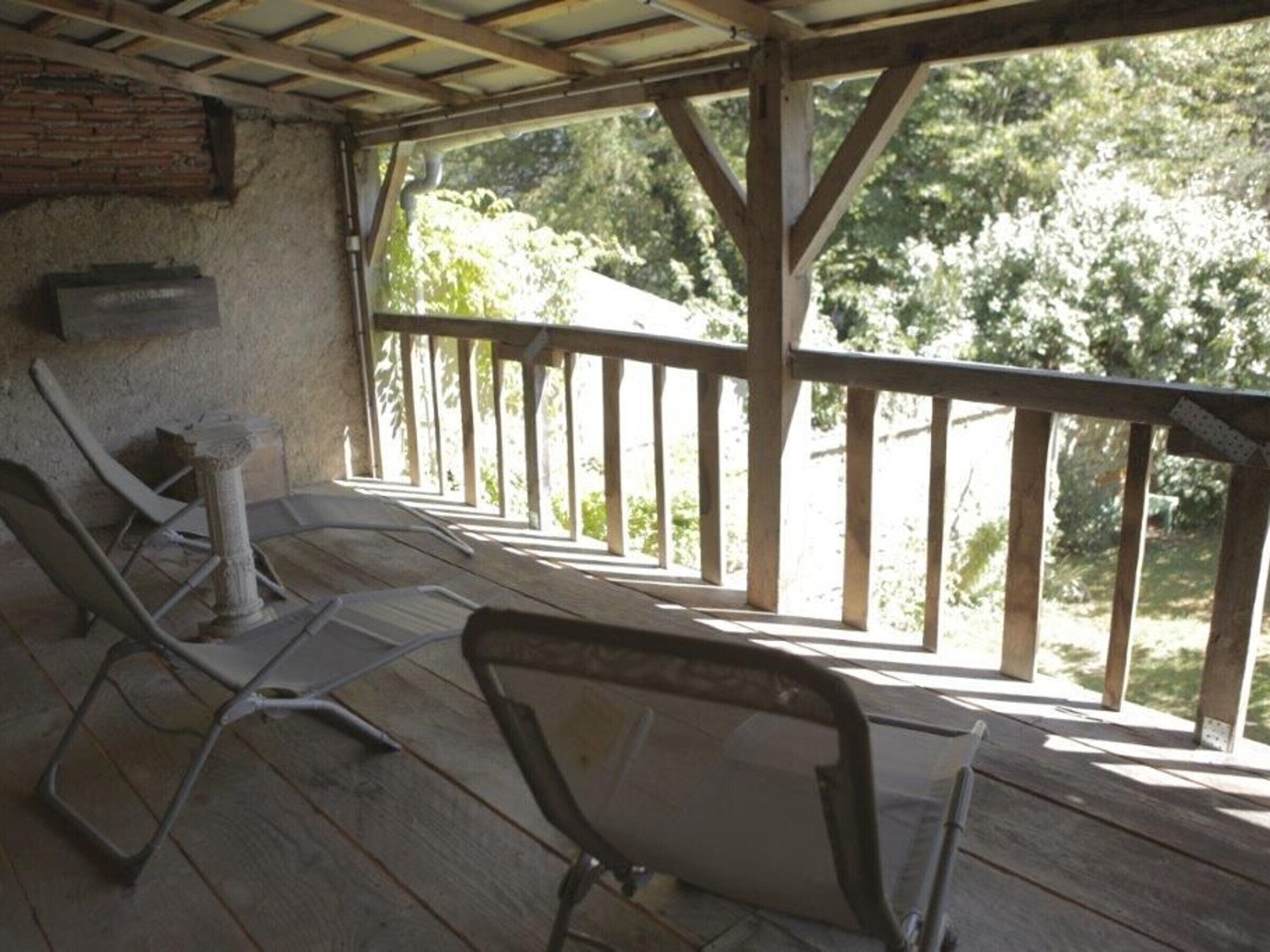 Un espace extérieur abrité, doté d’un plancher en bois et d’une rambarde, comprenant deux fauteuils et une petite table.