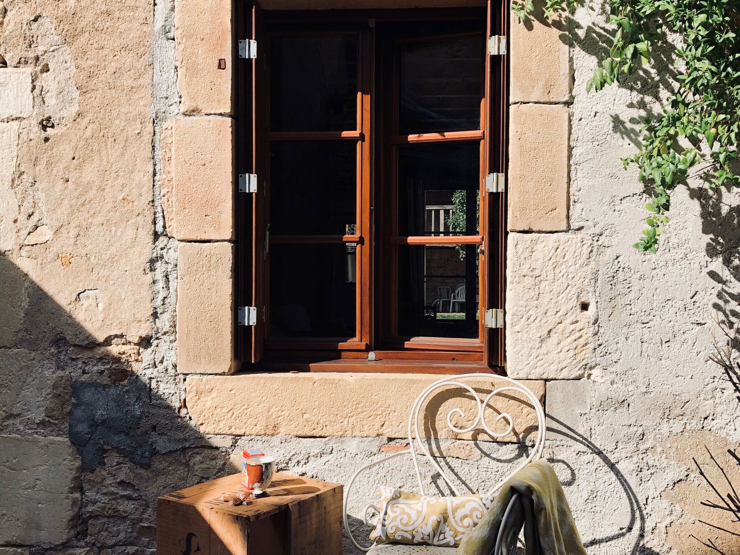 A rustic building with a wooden door and window, a metal chair, and a small table with a can.
