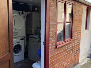 A laundry room with stacked washing machines, a drying rack, and a window with a brick wall. - Cozy lodging in city center - 8 guests (Saint-Amand-Montrond)