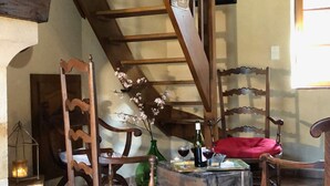 Une pièce chaleureuse avec une échelle en bois, une chaise dotée d’un coussin rouge et une table sur laquelle se trouvent une bouteille et des verres.