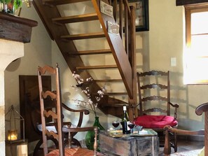 Une pièce chaleureuse avec une échelle en bois, une chaise dotée d’un coussin rouge et une table sur laquelle se trouvent une bouteille et des verres.