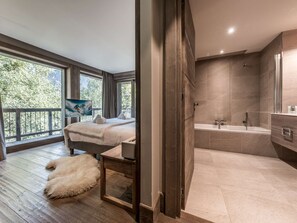 Ein modernes Schlafzimmer mit einem großen Bett, einem Fernseher und Blick auf Bäume durch das Fenster.