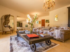 Ein Wohnzimmer mit einer Couch, einem Couchtisch mit Büchern, einer Vase mit Blumen, einer Chandelieber und einem Essbereich im Hintergrund.